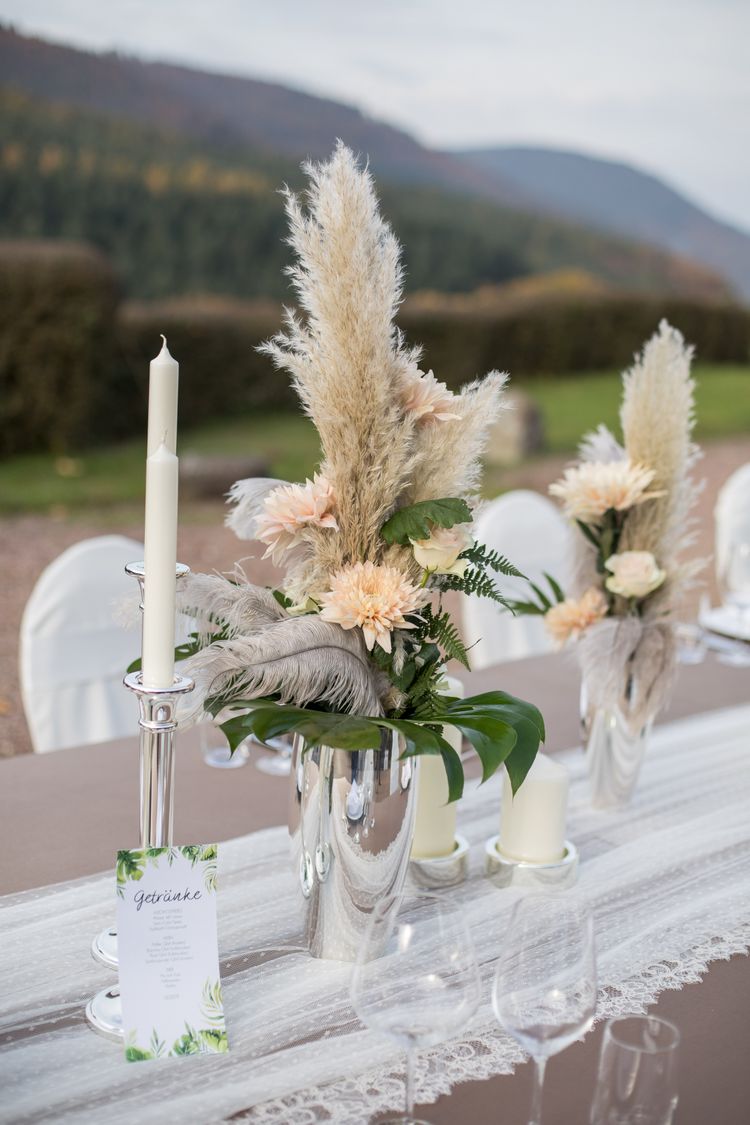 Silberne Vase mit apricot farbenen Blumen, Federn und Blattgrün
