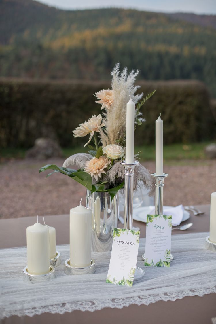 Silberne Vase mit apricot farbenen Blumen, Federn und Blattgrün, Spitzentischdecke, personalisierter Wein, silberne Kerzenstände