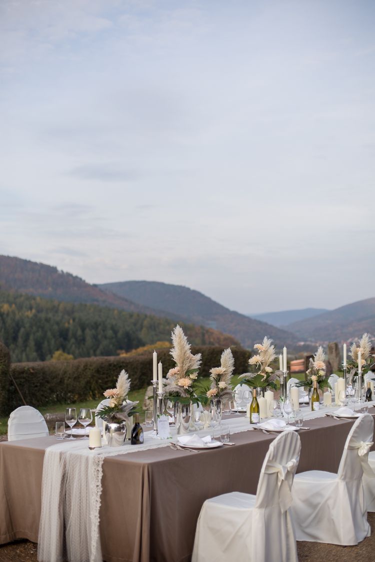 Silberne Vase mit apricot farbenen Blumen, Federn und Blattgrün, Spitzentischdecke, personalisierter Wein, silberne Kerzenstände