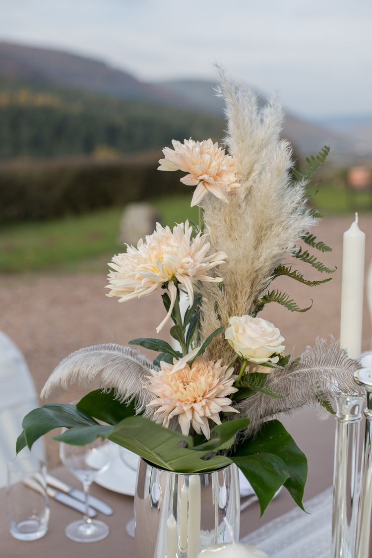 Silberne Vase mit apricot farbenen Blumen, Federn und Blattgrün, Spitzentischdecke, personalisierter Wein, silberne Kerzenstände